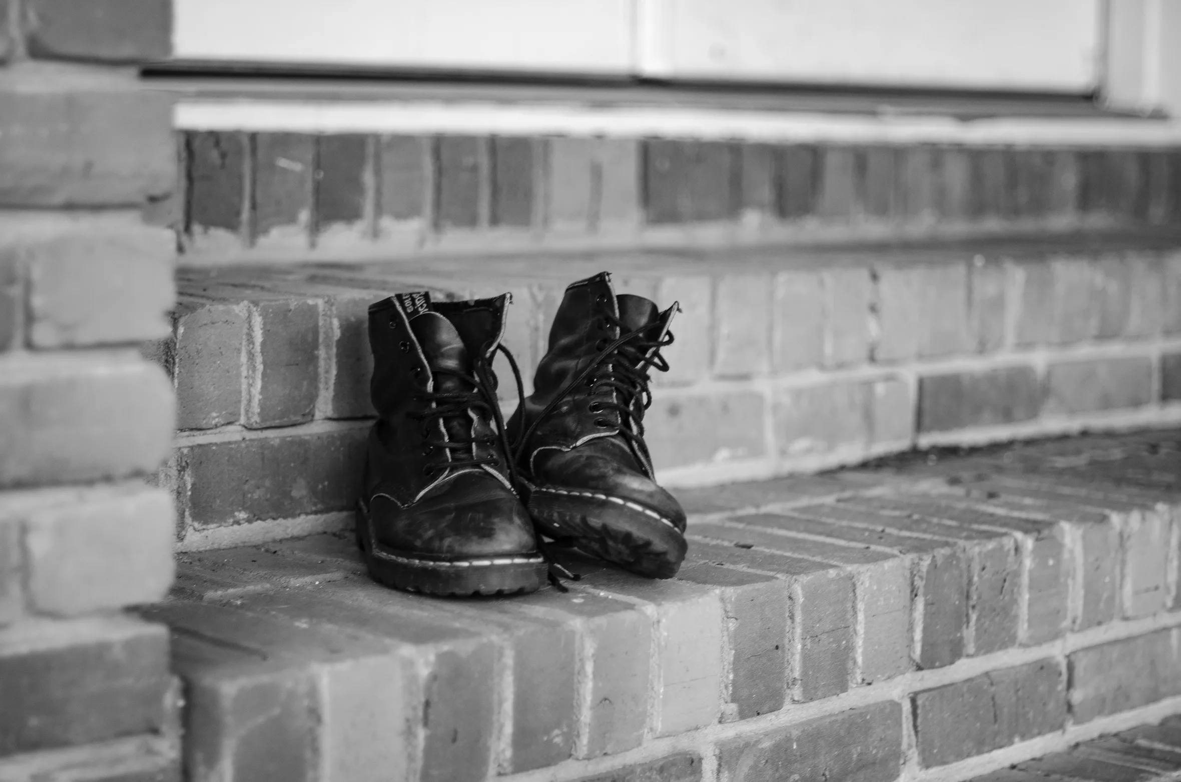 A close-up of black boots upon a brick step outside a door.