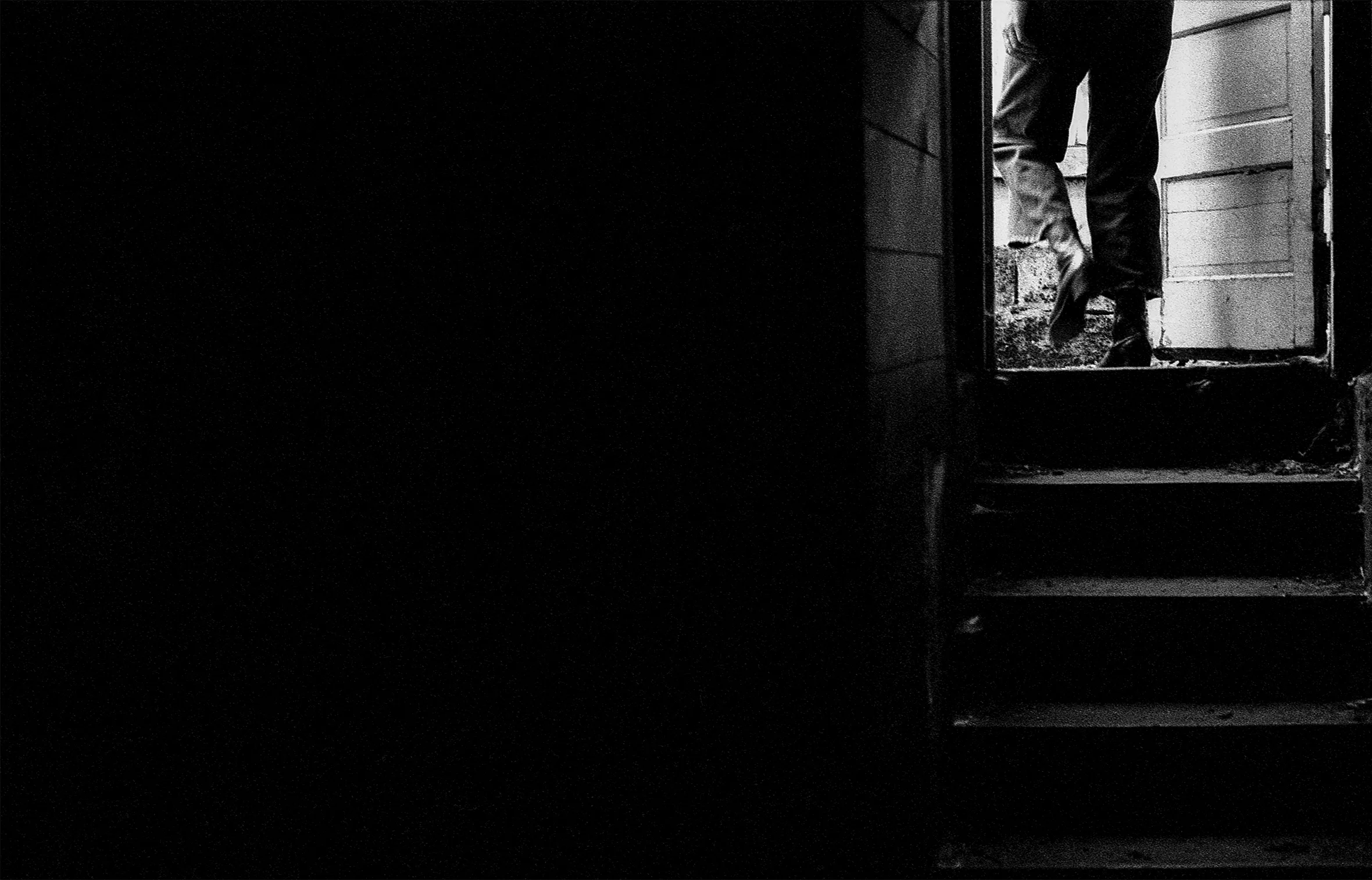 A person in jeans and boots walks through the doorway of a building after climbing a short flight of stairs.