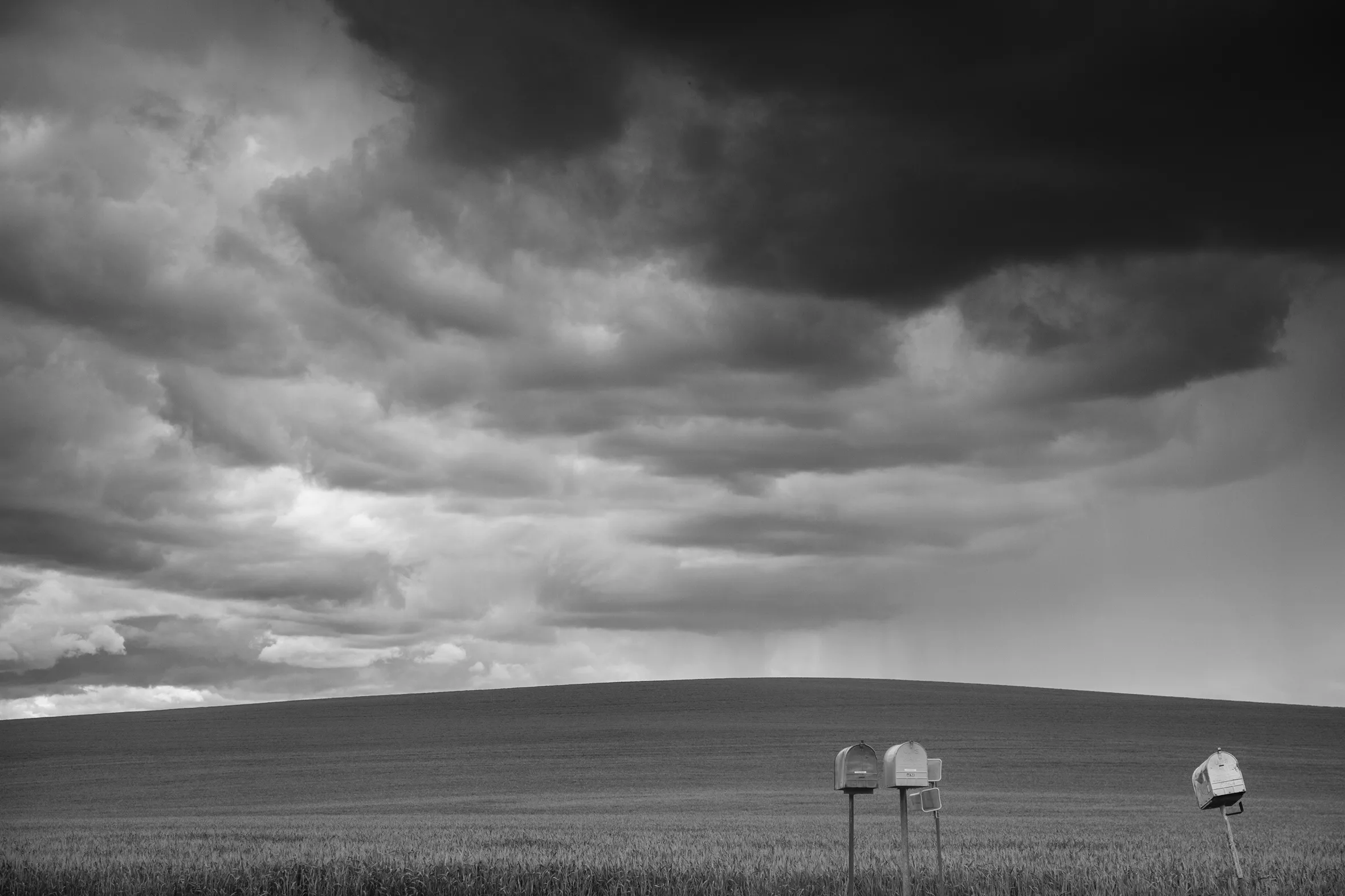 A few post-mounted mailboxes on a desolate stretch with nothing but field to the horizon below cloudy skies.