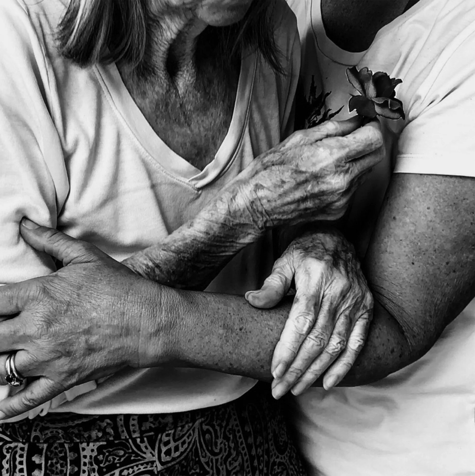 Close-up of the torsos of an elderly woman standing and holding a flower and a younger woman who steadies her.