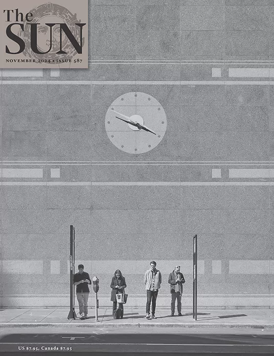 Issue 587 Cover November 2024 cover of The Sun. Four people wait for a bus on Pine Street in San Francisco. Two men and a woman stand and look down at their phones and one man stands with his hands behind his back. The clock on the building behind them reads 3:50.