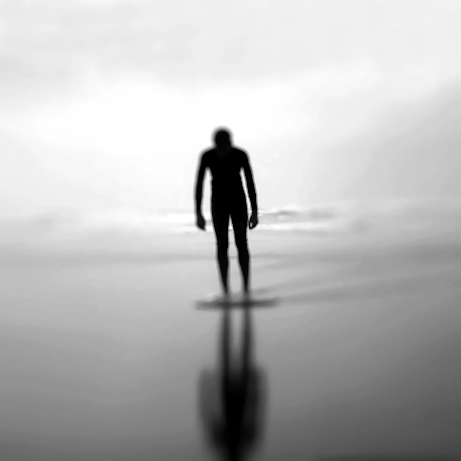 A silhouette of a hunched person standing on a beach
