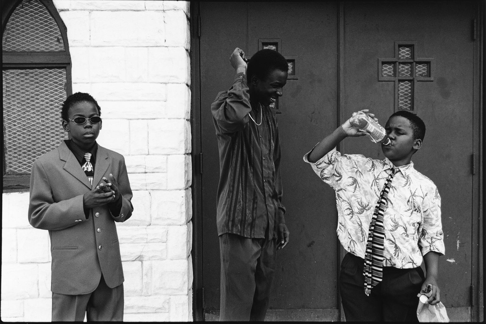 Three Black boys stand in front of the doors of a church