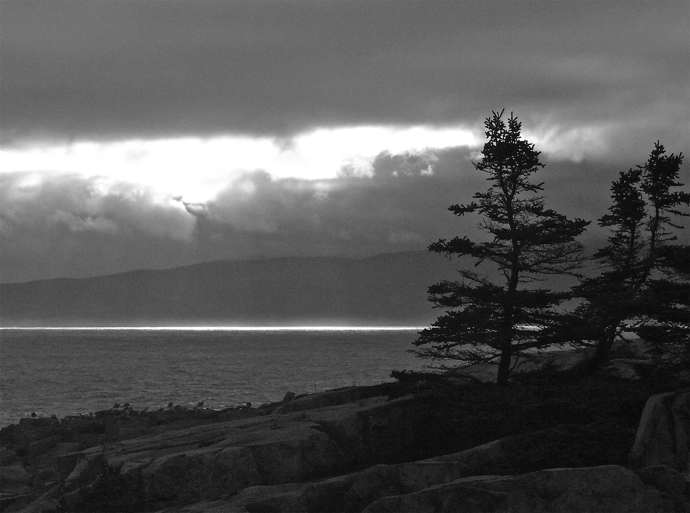 A sunlit line of water opposite a cliff with trees