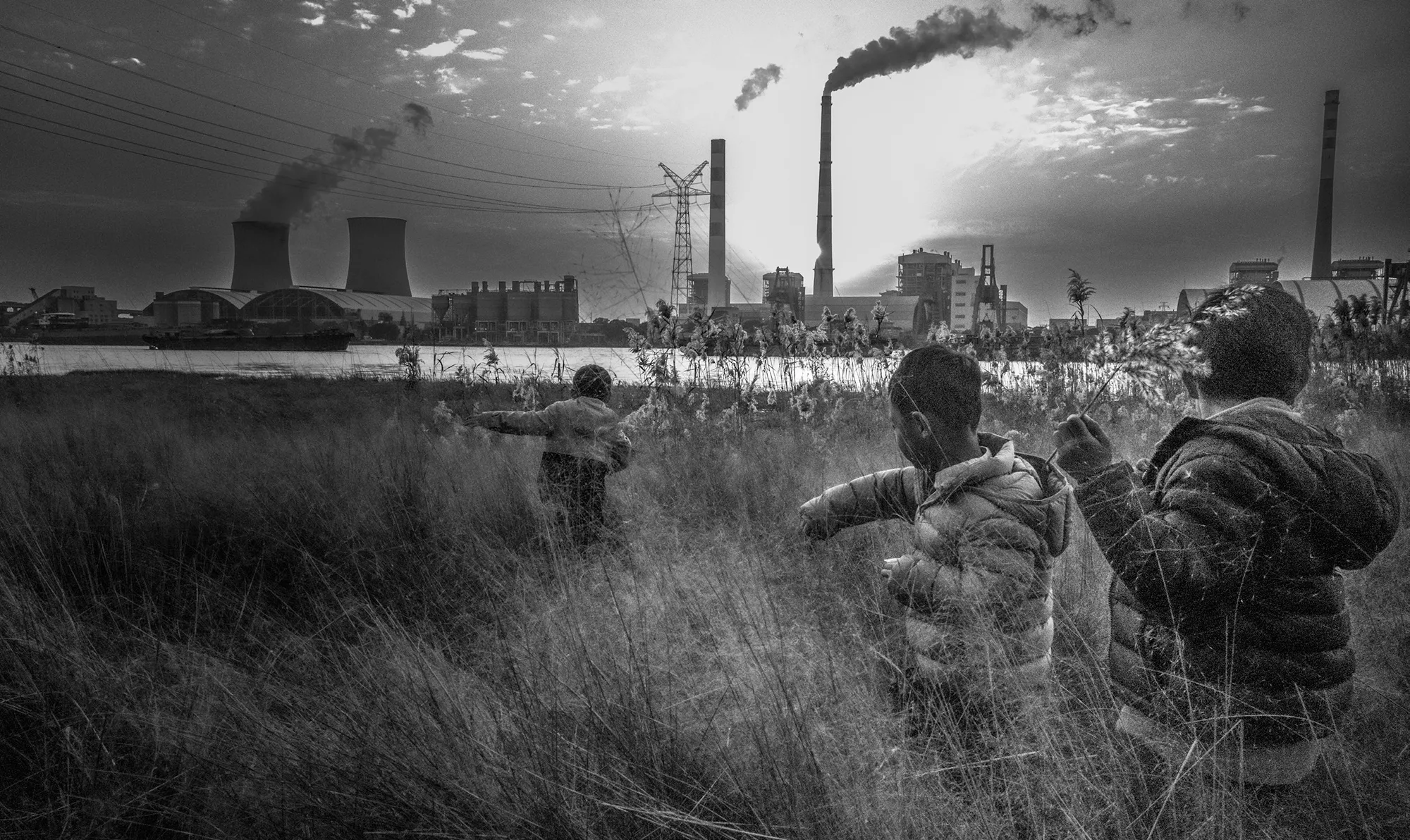 Children playing in tall grass across the river from a nuclear power plant