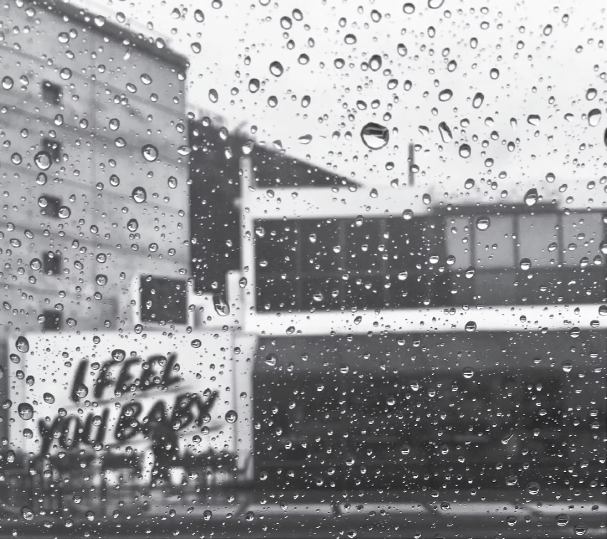 A view of buildings and "I feel you baby" sign through a rain-speckled window 