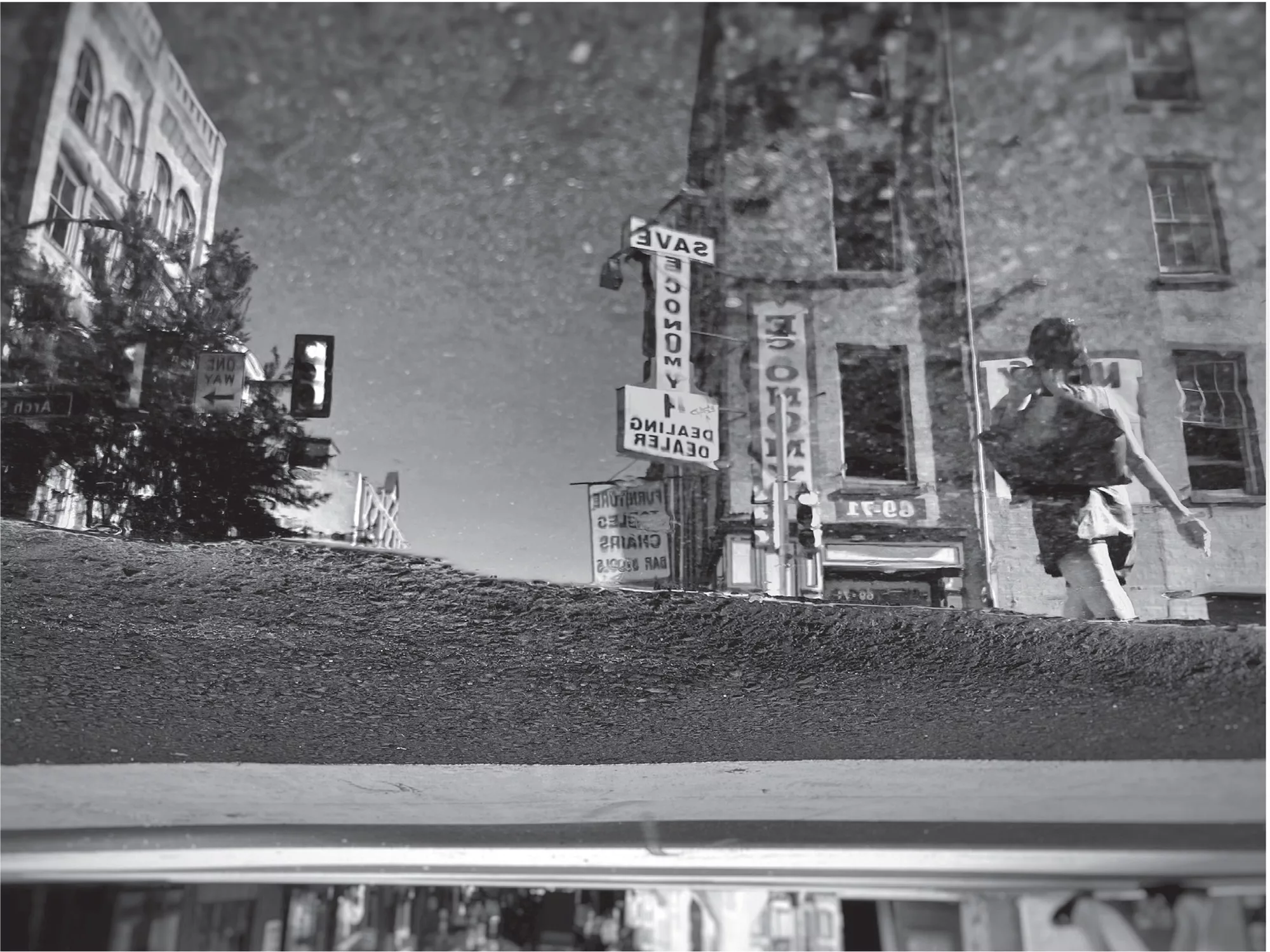 A reflection of buildings, a woman walking, and a SAVE ECONOMY sign in a puddle of water