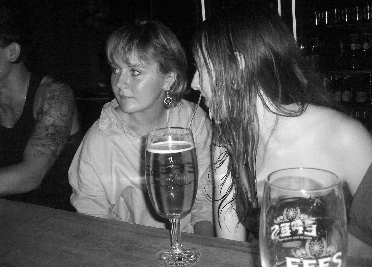 Two women sit with beers at a bar