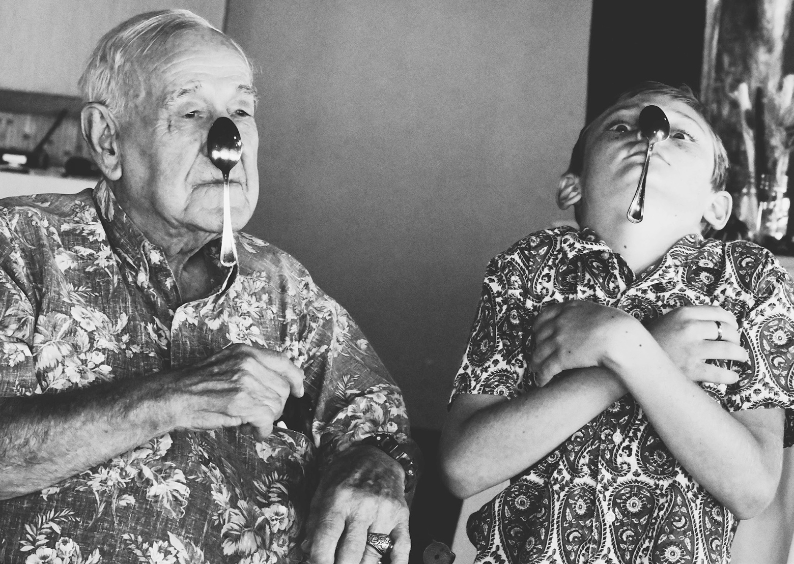 An older man and a boy balance spoons on their noses