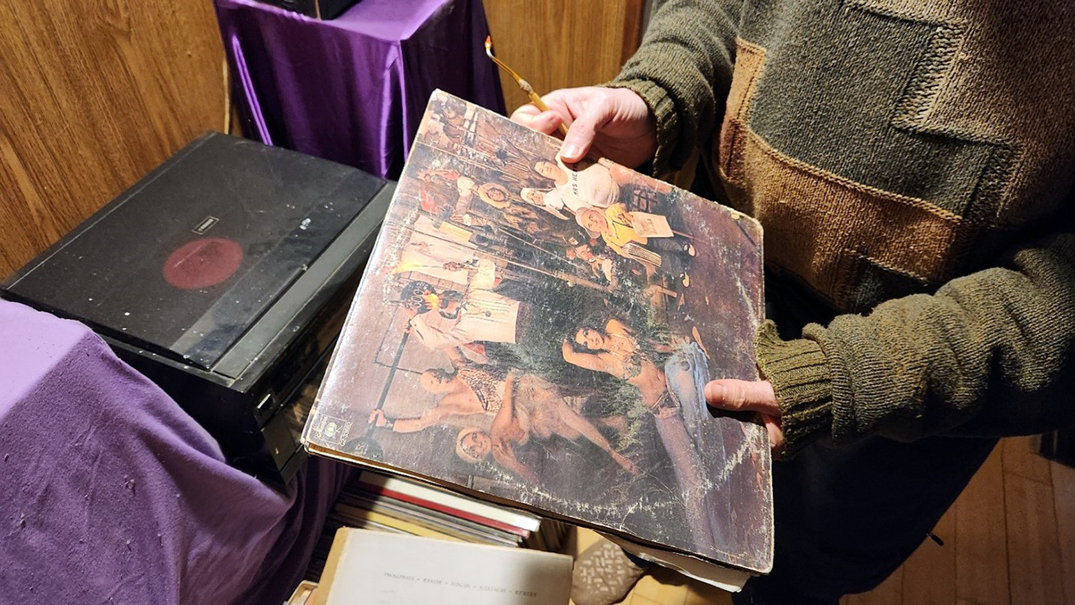 Sparrow holds the worn LP album cover of Bob Dylan & The Band's The Basement Tapes above a covered turntable. The album cover shows much wear and tear including a very noticeable record ring.