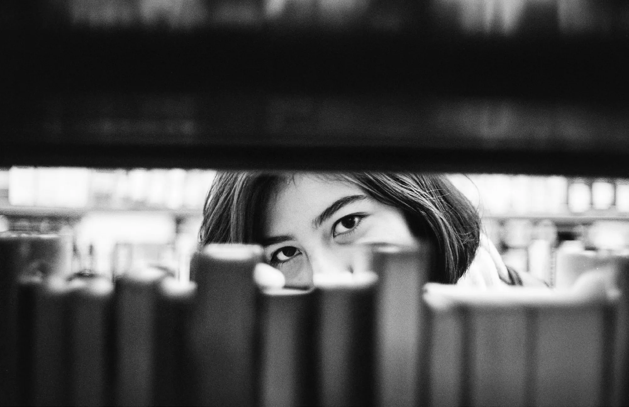 Woman peering through space in bookshelf