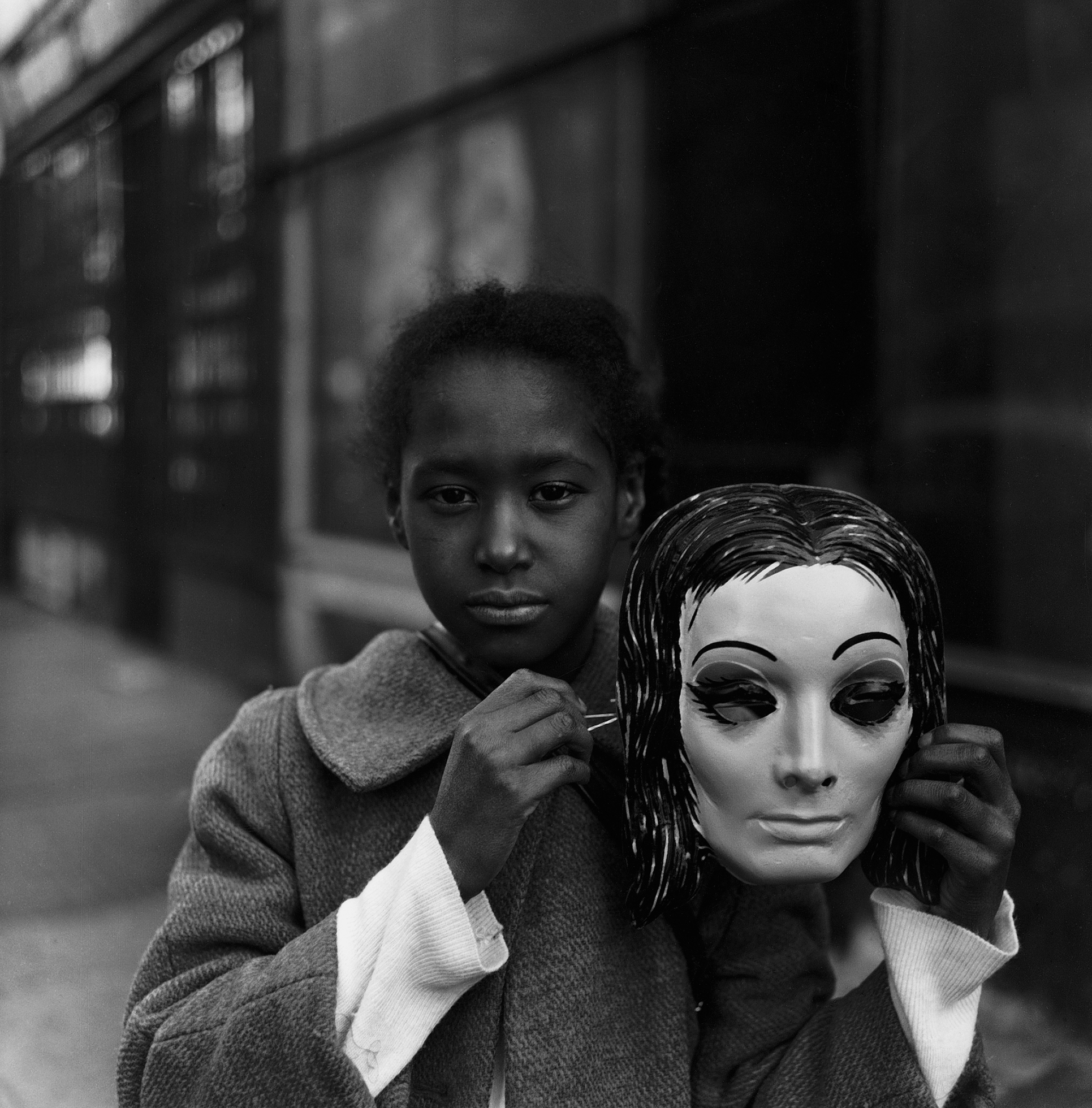 A Black girl holds a mask of a white face
