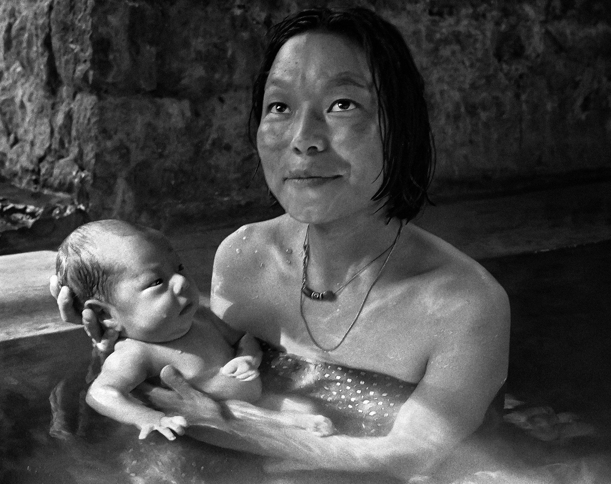 A Bhutanese woman looks up as she is sitting in a hot spring holding her baby.