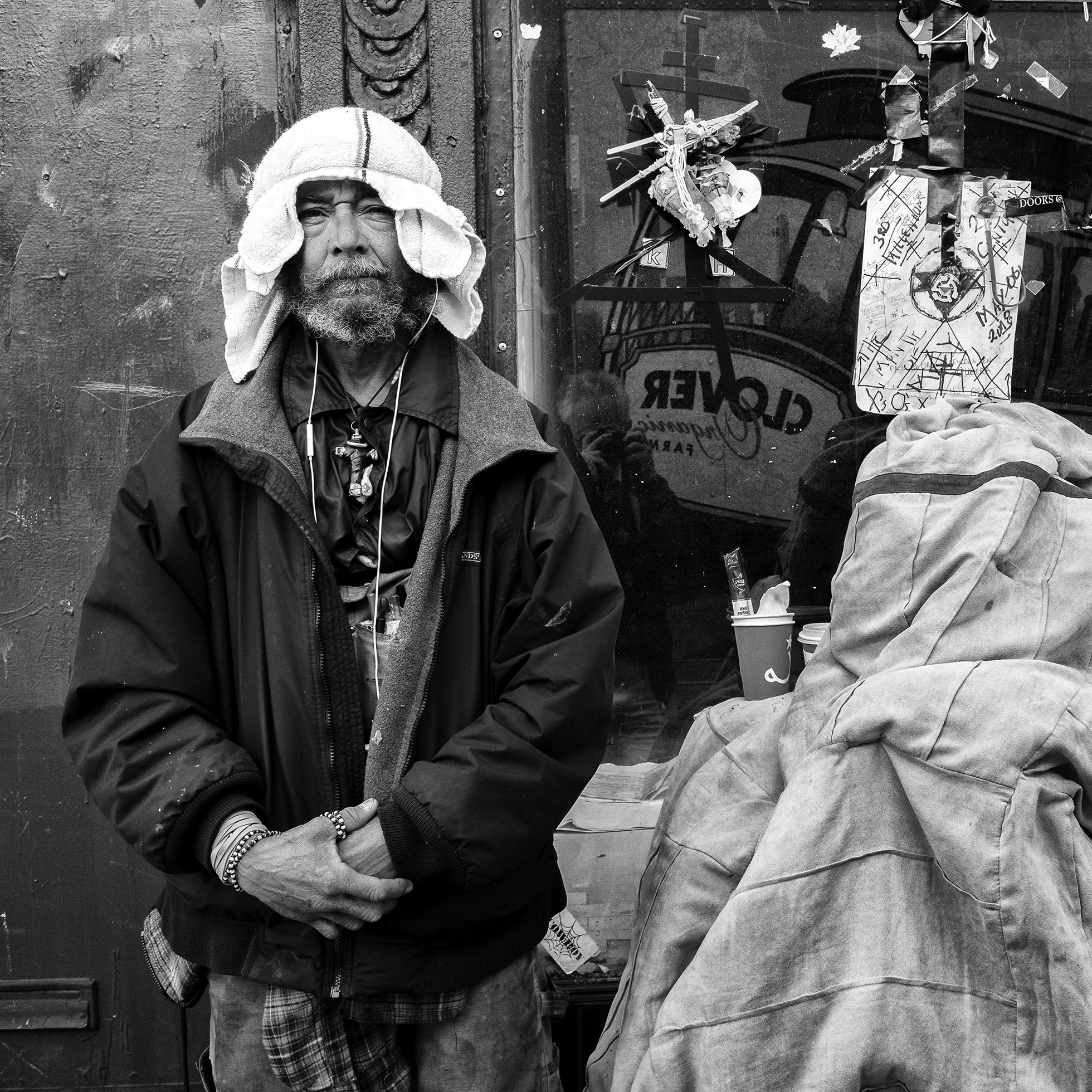 Joseph looks into the camera and stands with his arms clasped in front of him in San Francisco in May 2018. He is wearing a jacket, a large cross around his neck, and a head covering that cascades to his shoulders.