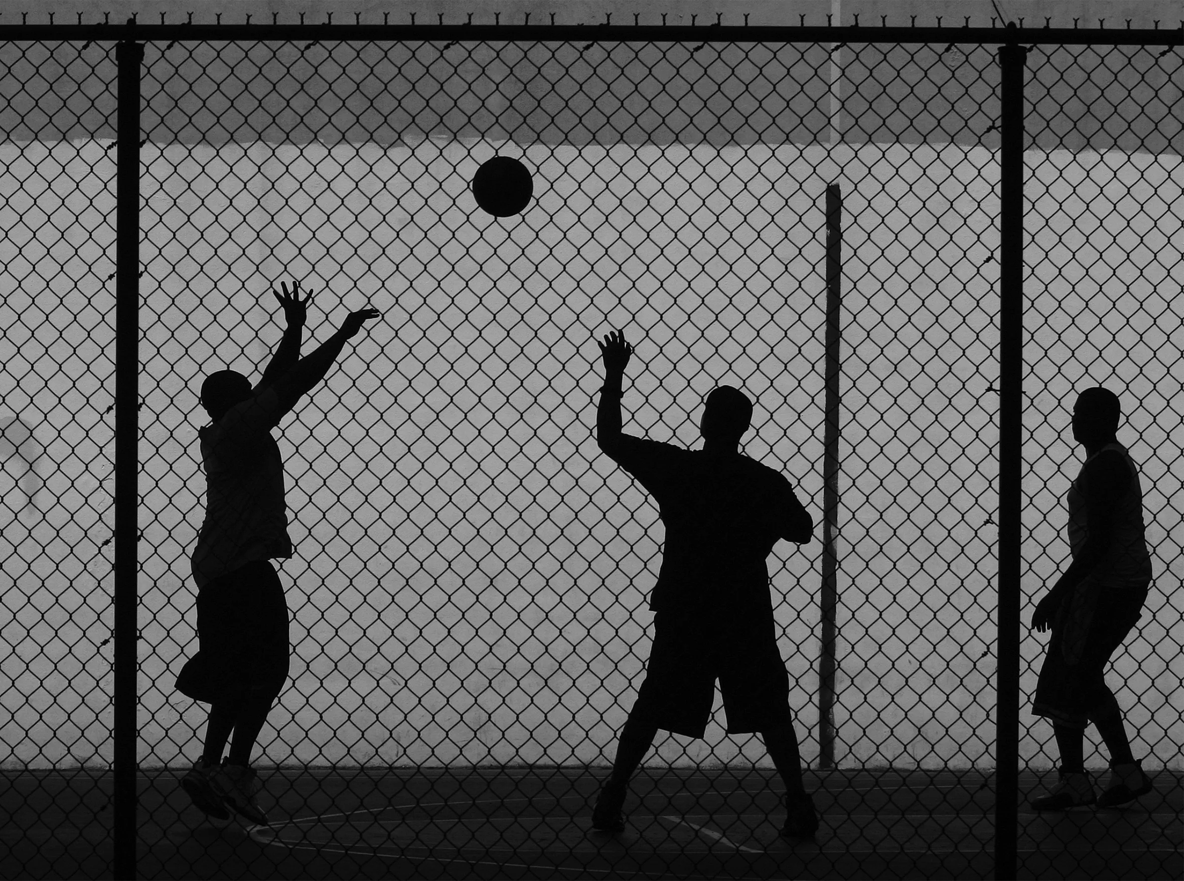 Three street ballers at a playground in Manhattan seen through a chain-link fence.